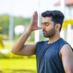 A young man doing nostril breathing or pranayama by closing his right nostril standing in an outside environment.