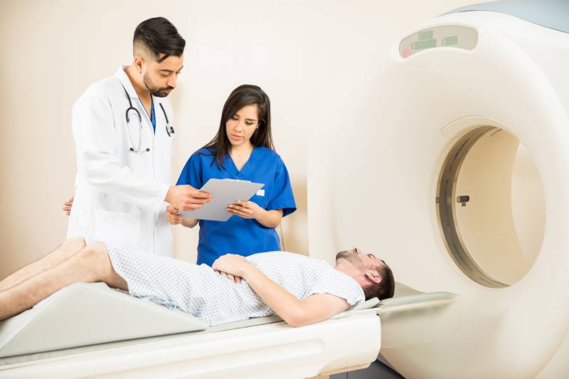 A male doctor and a female technician discussing the medical details of a patient lying on a CT scanner.