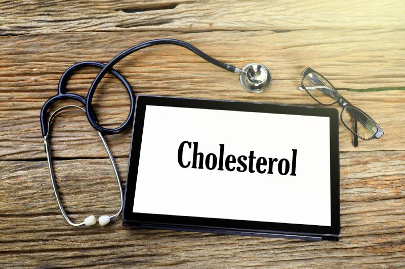 A stethoscope, a spectacle and a tab kept on wooden table with the word CHOLESTROL displayed on the tab.