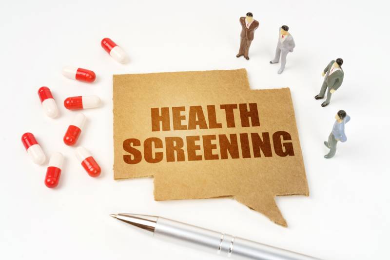 Image of pills, a pen, miniature figures of people, a sign with the inscription - HEALTH SCREENING shown on a white background.