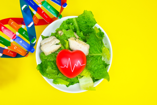 Healthy and nutritious food kept in a plate with a red coloured heart symbol kept on it and a multi coloured DNA strand with nutrition related terms mentioned on it.