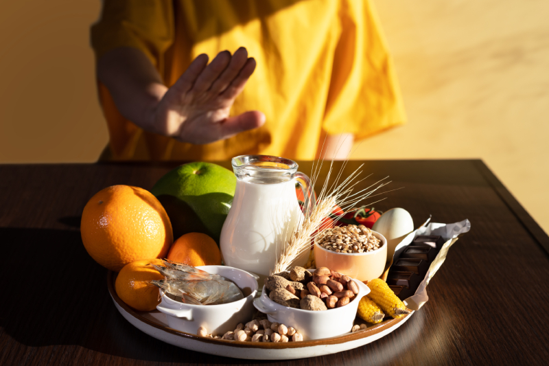 A woman avoiding food allergens - fish, seafood, dairy, peanuts, tree nuts, eggs, chocolate, wheat, soy and citrus fruits kept on a table.