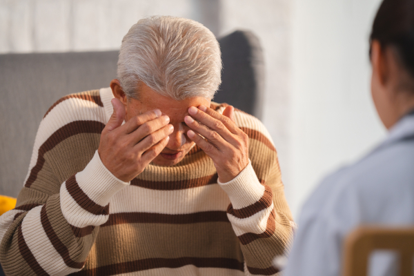 An elderly person sitting in front of a doctor/ a psychiatrist holding his head in a depressed state.
