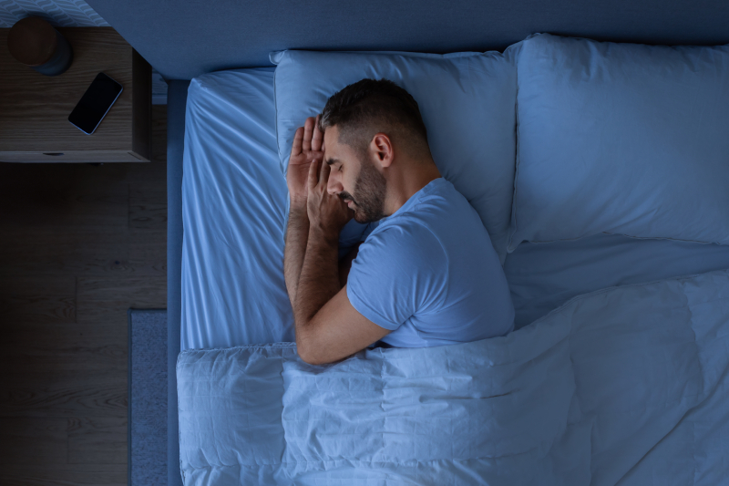 A person sleeping in his bedroom turning towards his right side and his hands kept under his face.