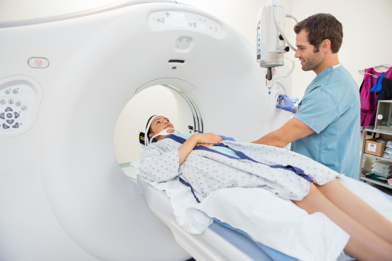 A male radiographer preparing a female patient lying on the CT scan table for a scan.