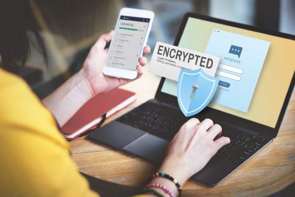 Side view of a woman using laptop and a mobile phone with an encrypted message and symbol before the desktop.