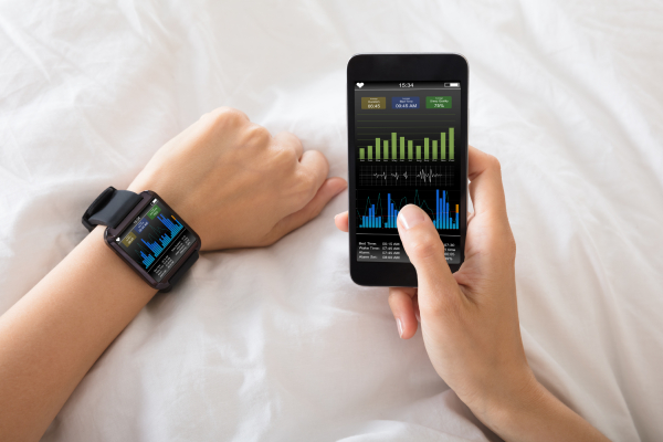 Close-up image of a female's hand with a smart watch and mobile phone both showing heart beat rate.