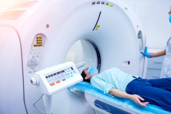 Side view of a CT room with a radiologist and a female patient lying on the scanning table.