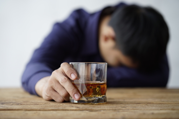 Blurred image of a person lying his head down on a table with his right hand holding a glass filled with alcohol.