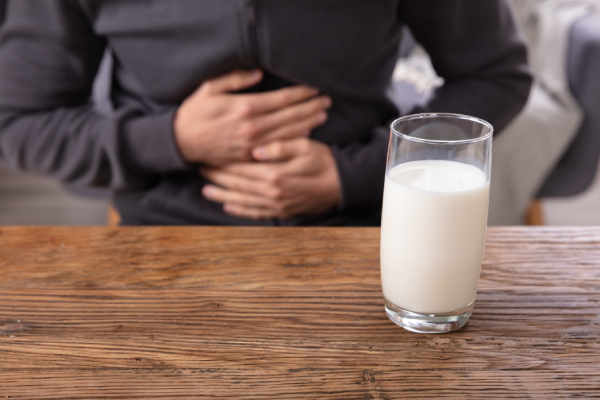Midsection view of a man suffering from stomach pain and a glass of milk kept on a table in front of him indicating milk intolerance.