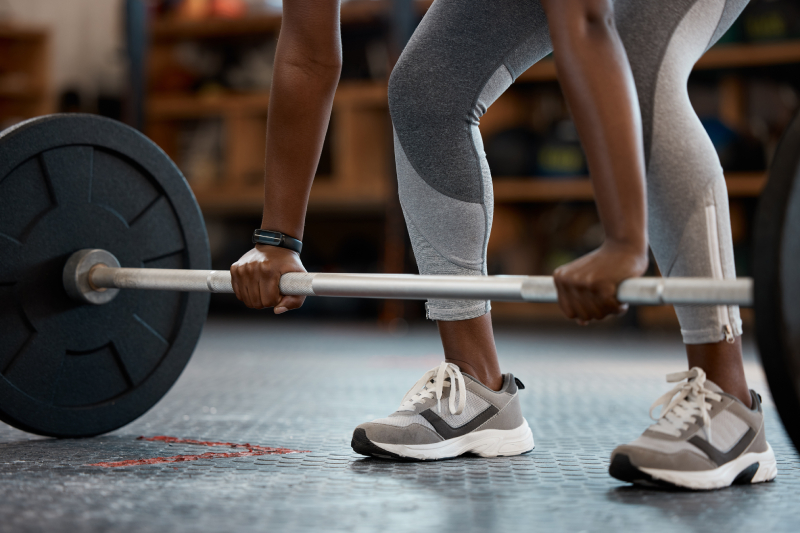 A fitness oriented female bodybuilder or a weightlifter trying to lift a barbell inside a gym or exercise room.