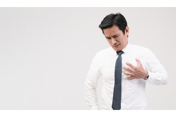 A person standing in front of a white background holding the left side of his chest with severe pain visible on his face.