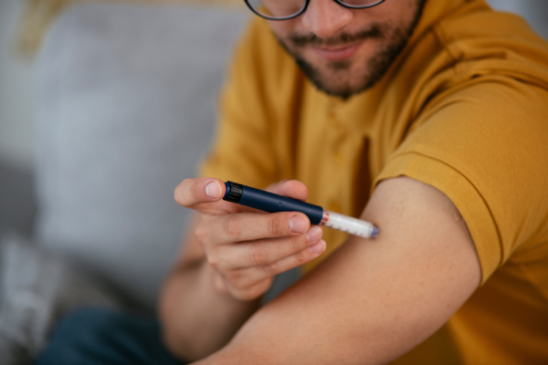 Image of a young man giving himself an insulin shot on his left hand using an insulin pen.
