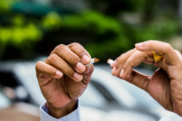 Close up view of two hands breaking a cigarette into two parts on a blurred background.