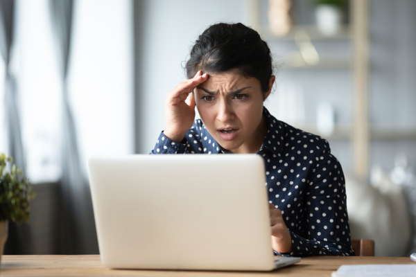 Image of a shocked and confused looking woman reading an unhappy news looking at laptop sitting in a home.