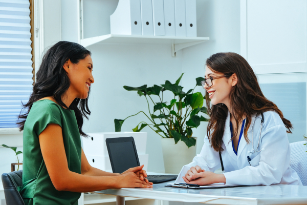 Female doctor and patient having a warm interaction sitting inside a pleasant white themed consulting room.