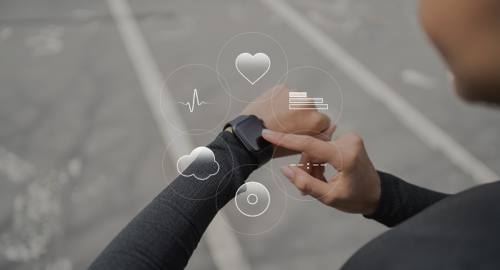 Image of an athlete wearing a smart watch on her hand touches the screen with the other hand and virtual images related to a fitness app displayed in the middle of the image.