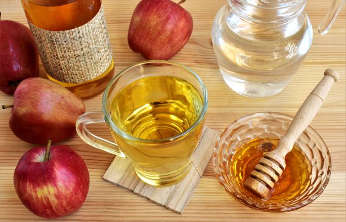 Apple cider vinegar with honey, water and few apples kept on a wooden table.
