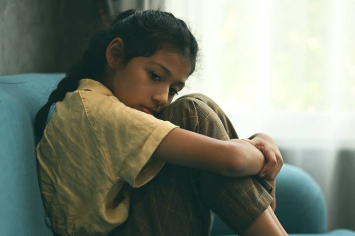 An upset girl sitting on a sofa hugging her knees.