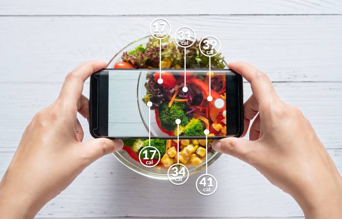 A mobile held above a salad bowl displays the calories of each ingredients on its screen.