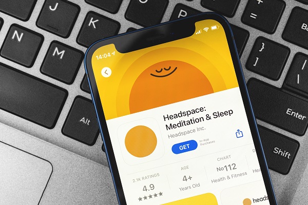 Close up top view of a mobile placed on a laptop keyboard with headspace meditation and sleep app displayed on the mobile screen.