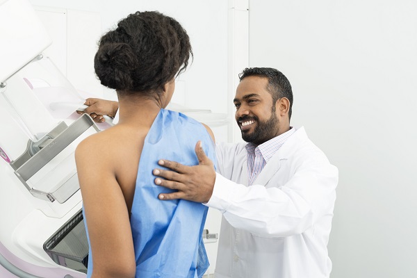 A male doctor assisting female patient undergoing mammogram.