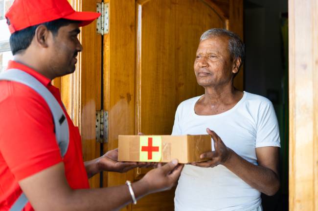 A senior citizen receives a package of online-ordered medication from a delivery person at home.