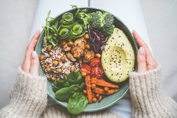 Top view of a woman, sitting with a bowl of healthy plant based food kept on her lap and her hands holding the bowl.