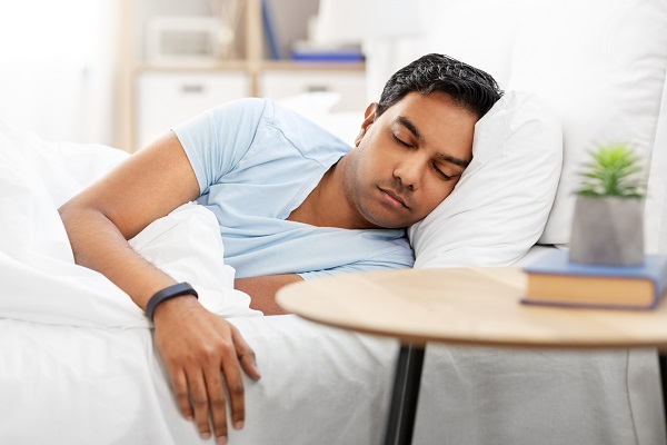 Image of a person sleeping peacefully inside his white themed bed room wearing a smart watch.