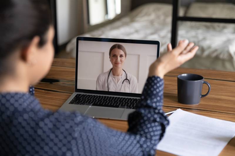 A woman speaks to her doctor through video conferencing on a laptop.