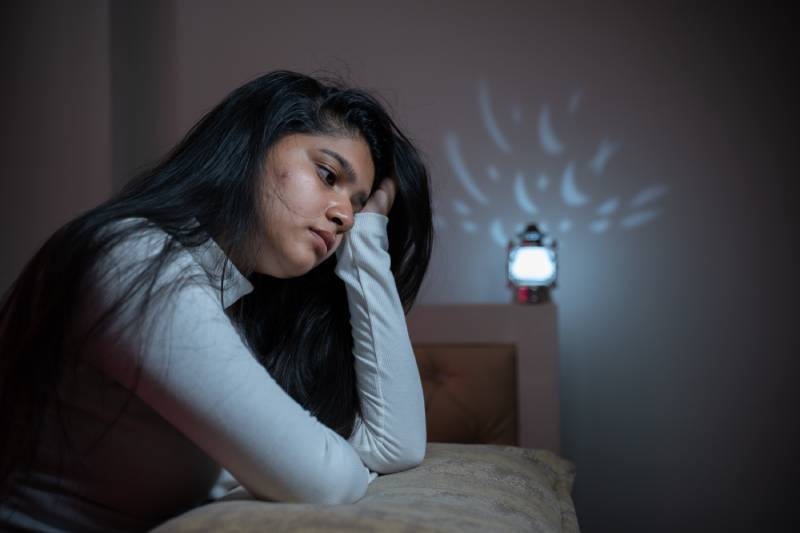 A young girl, feeling anxious, wakes up at night in her bed.