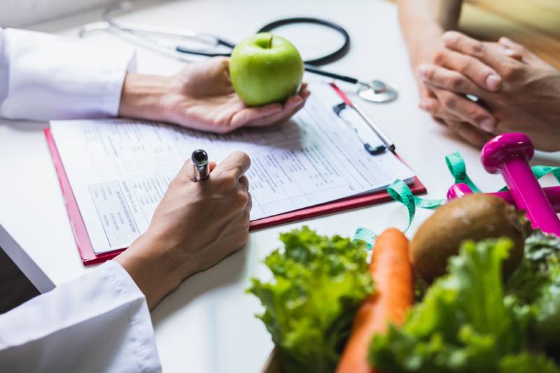 A nutritionist giving consultation to a patient with healthy fruit and vegetables on the table.