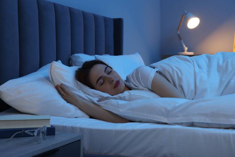 A woman sleeping peacefully in her bedroom with the bed lamp on.