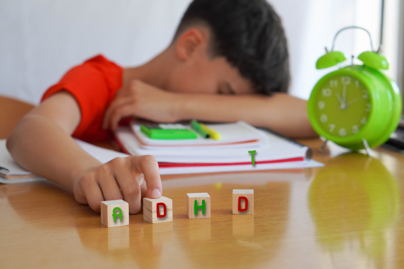 A young boy, surrounded by books and notebooks, looks frustrated, symbolizing Attention Deficit Hyperactivity Disorder (ADHD).