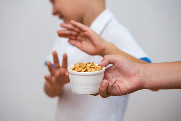 A person offering a cup of nuts to a boy who refuses due to a skin allergy.