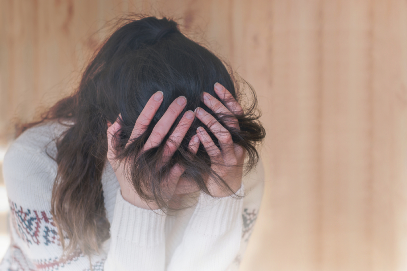 A woman holding her head in her hands, appearing stressed or overwhelmed due to OCD (Obsessive-Compulsive Disorder).