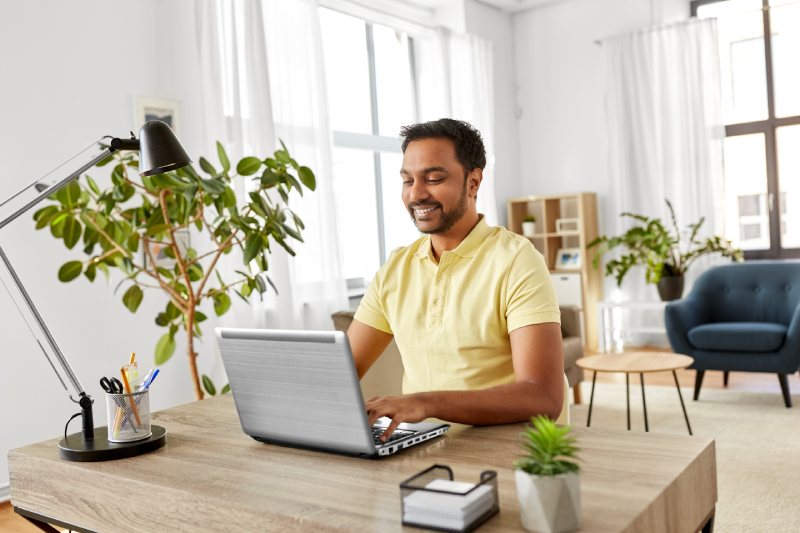 The man arranges a comfortable home office as he works remotely on his laptop.