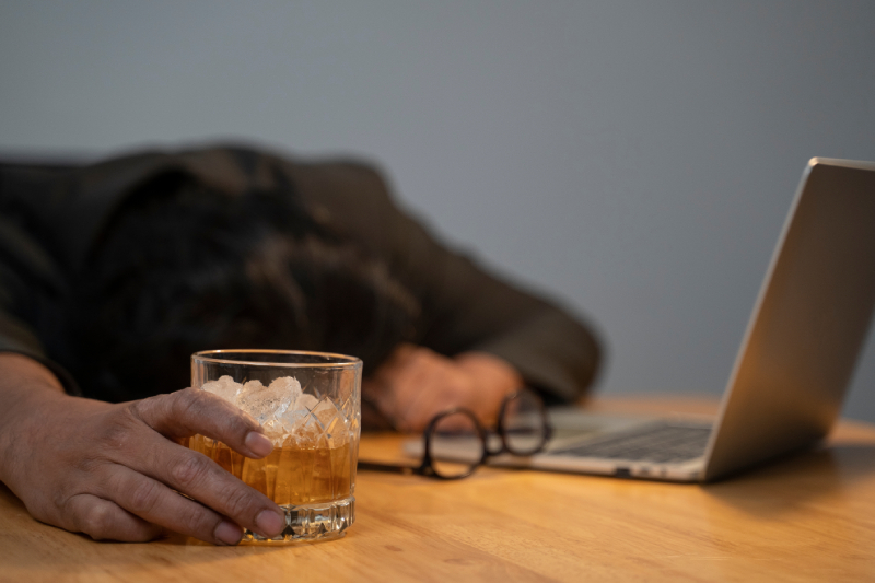 A person with depression and anxiety drinking alcohol at work illustrates the connection to potential alcohol addiction.