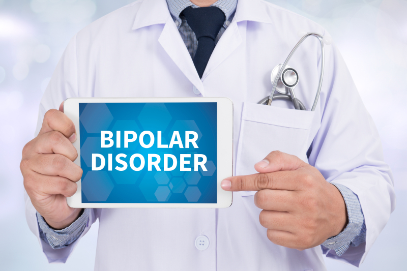 The doctor is holding a tablet displaying the text 'Bipolar Disorder,' with a stethoscope visible in the pocket.