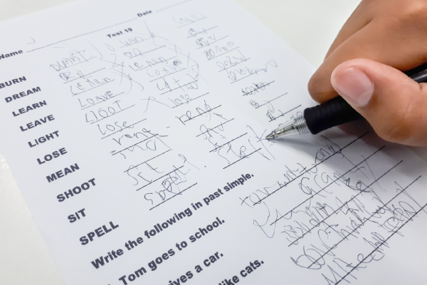 A student writes irregular verbs with unclear handwriting, highlighting the impact of brain impairment on evaluative processes.