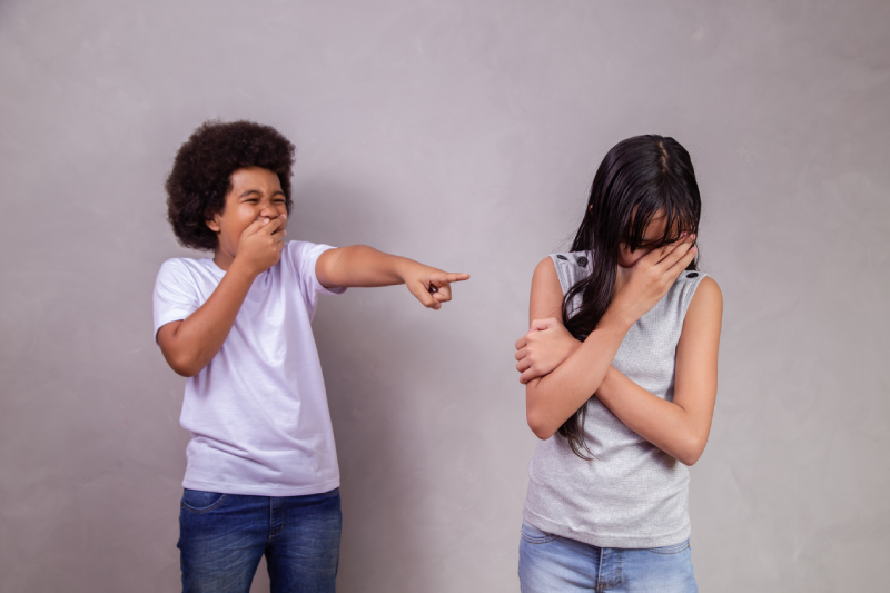 As a boy bullies a sad girl in the background, she covers her face with her hand.
