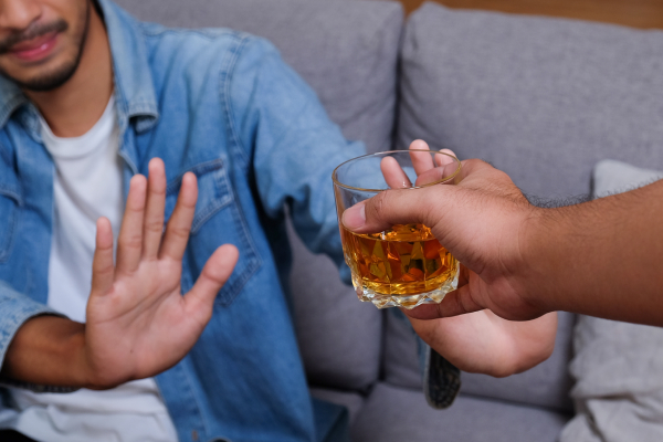 A man in a blue jean jacket signals refusal to alcohol, showcasing self-control as a way to avoid negative consequences.