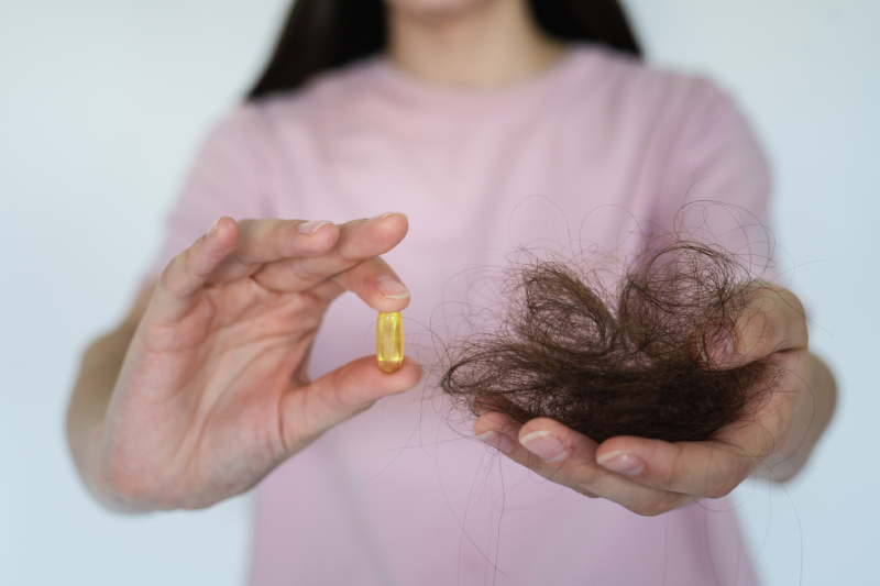 A girl in a pink T-shirt holds a handful of fallen hair, suggesting a vitamin deficiency.