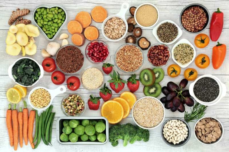 Fruits, grains, and seeds are arranged colorfully, representing the need for proper vitamin intake in a healthy, balanced diet.