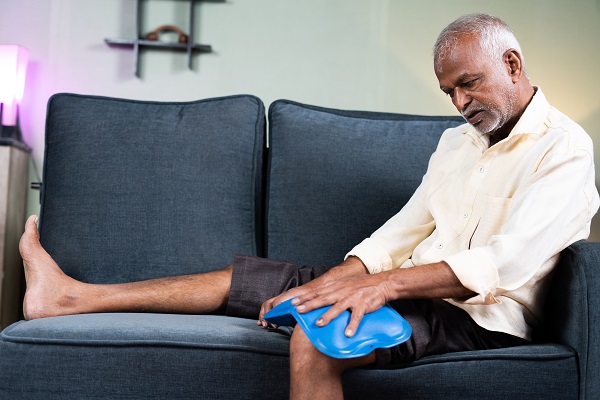 A senior man using a hot/cold pack on his leg to manage diabetic foot pain, sitting comfortably on a sofa.