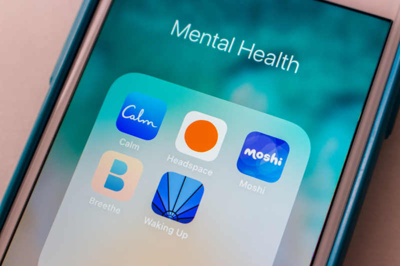 The smartphone screen shows a 'Mental Health' folder with the Calm, Headspace, Waking Up, and Moshi apps for well-being.