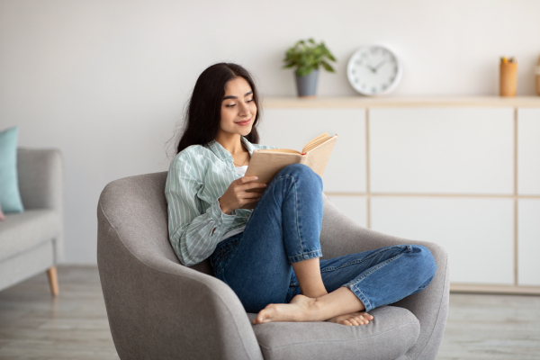 Happy young woman reading a book, illustrating an alternative to emotional eating for stress relief and mood improvement.