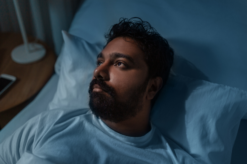 A sleepless man in bed, illustrating the challenge of finding the right treatment center for effective care of sleep disorders.