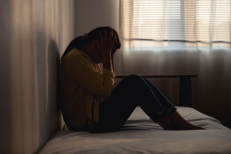 A woman sitting alone on her bed symbolizes the mental health challenges linked to post-traumatic stress disorder.