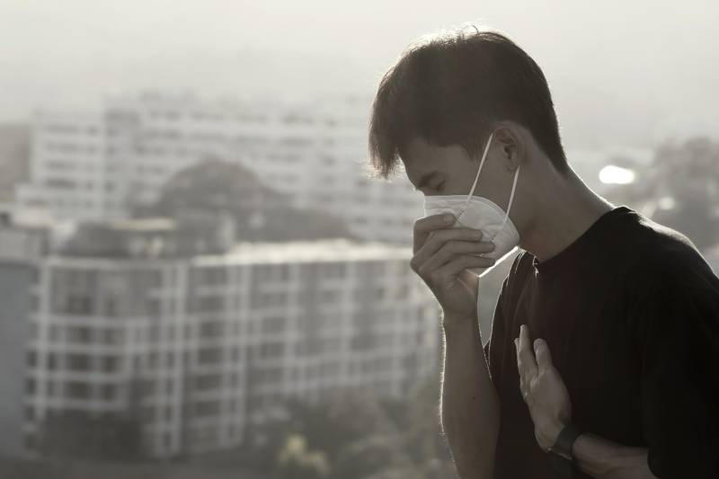 A man in a face mask outside with a cityscape, illustrating air pollution's impact on heart health.